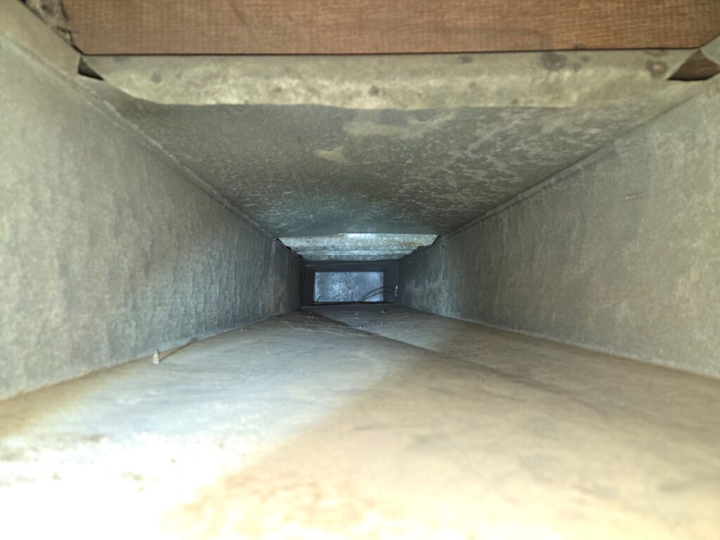 Inside view of a rectangular metal duct, showing a long, open channel, with wooden framing above.
